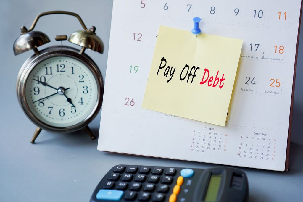 pay off debt concept with remind note on calendar with clock and calculator on desk