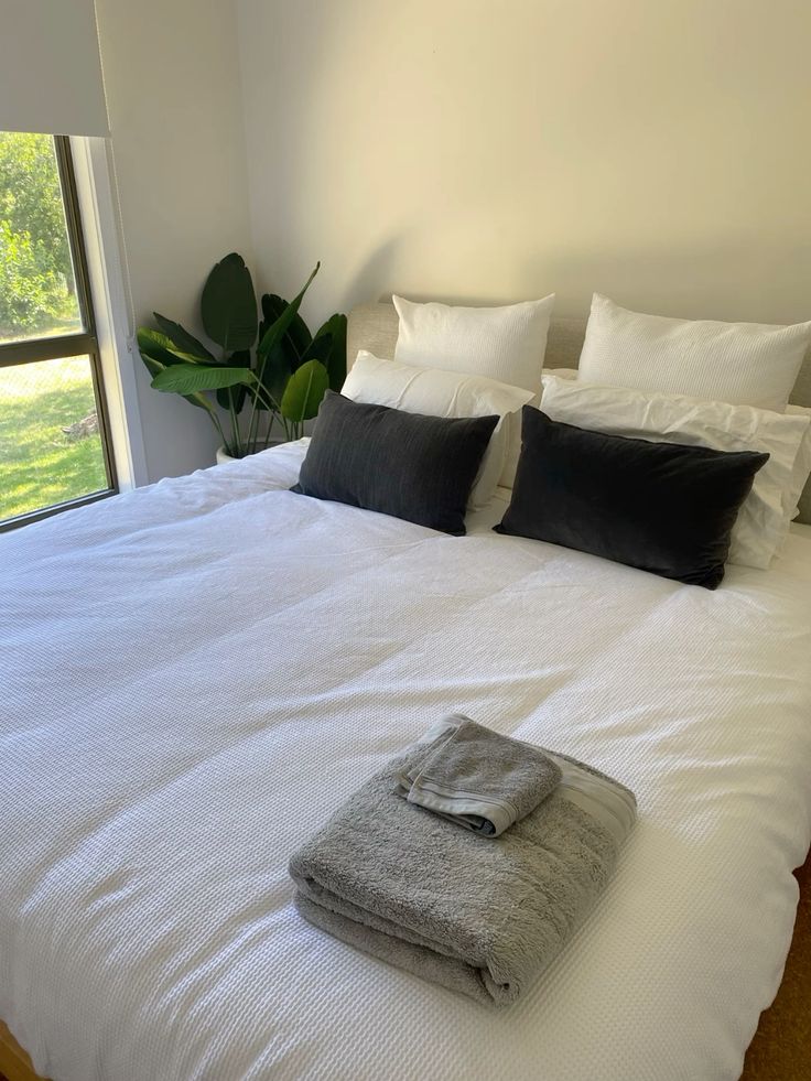 A neatly made simple bed with a set  of towel placed nearby
