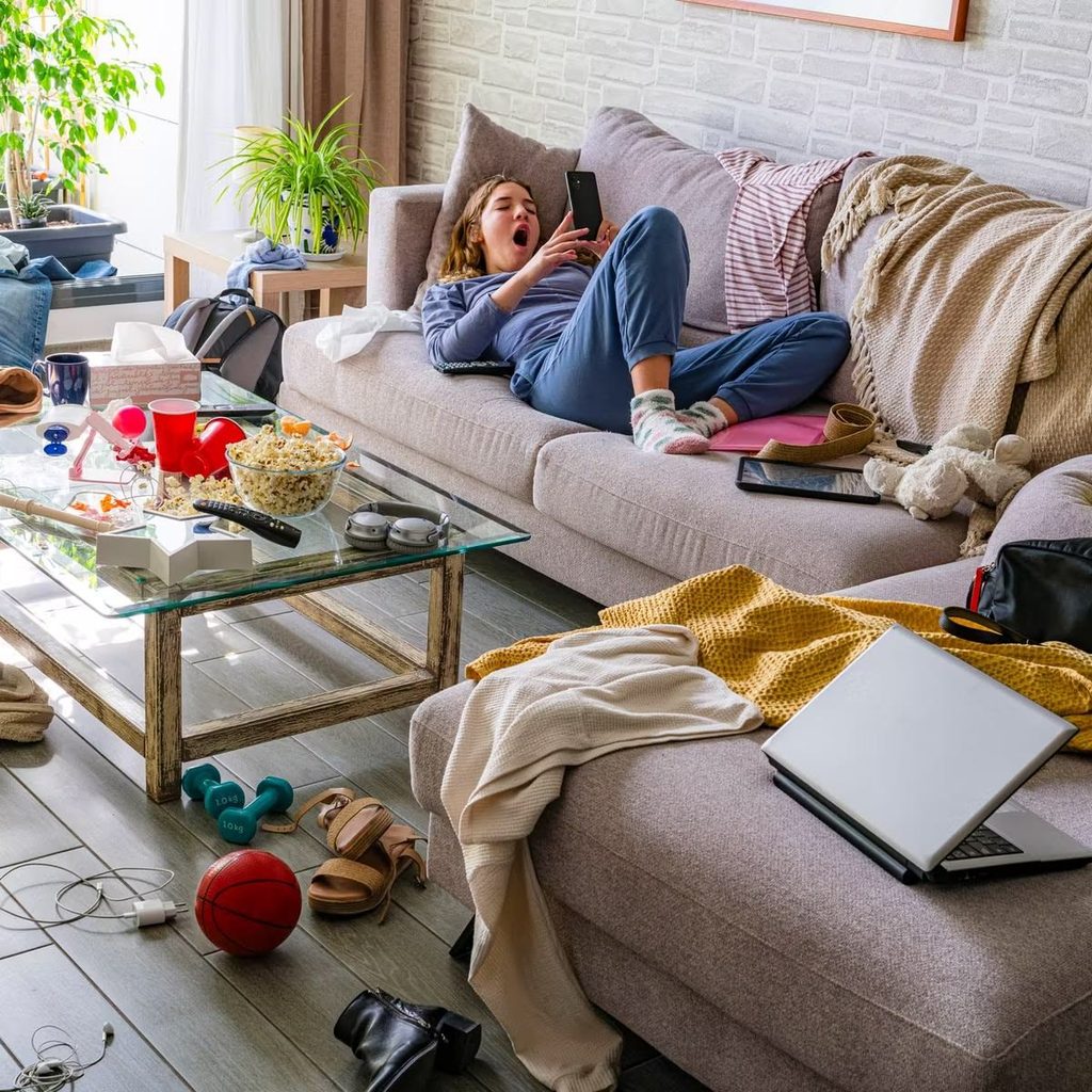 A person lying down on a couch in an unkept apartment   as regards to first week living alone