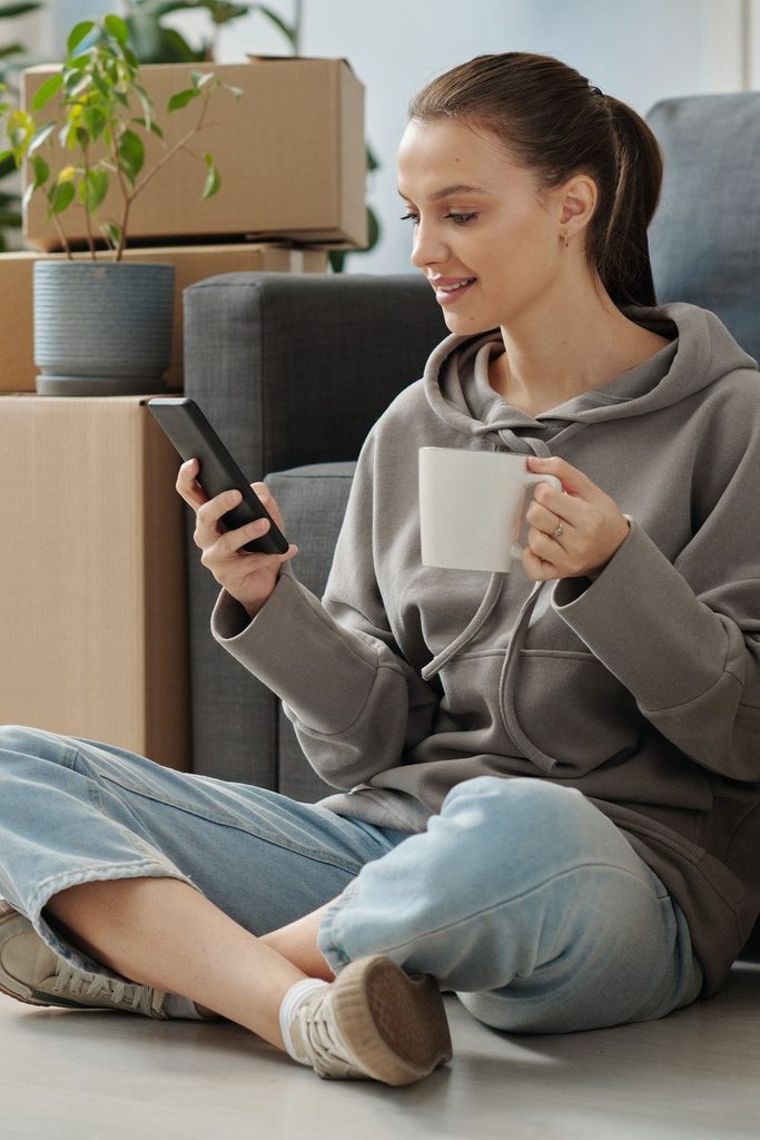 A tired but happy renter relaxing on the floor of a new apartment with a drink and a few unpacked boxes