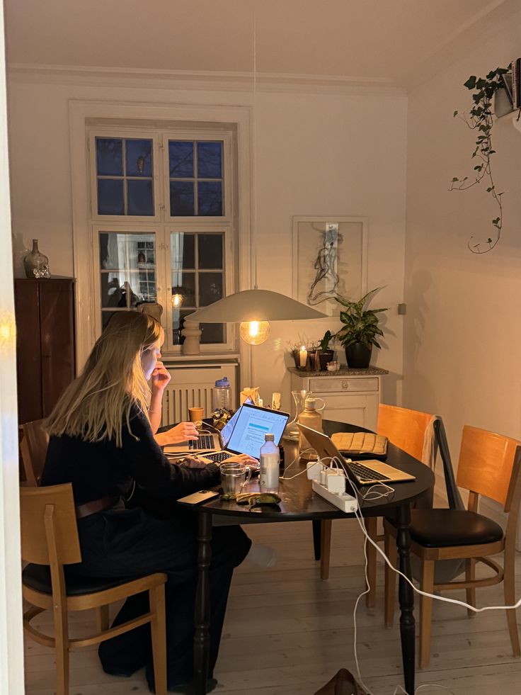 A young adult sitting at a small table in an apartment,  while using a laptop