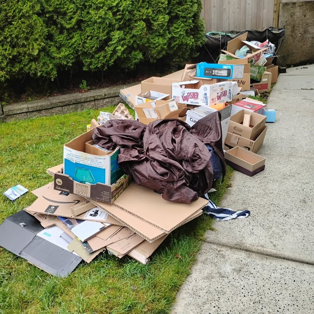 Flattened cardboard boxes, recycling bags, and moving rubbish neatly arranged beside an apartment bin area