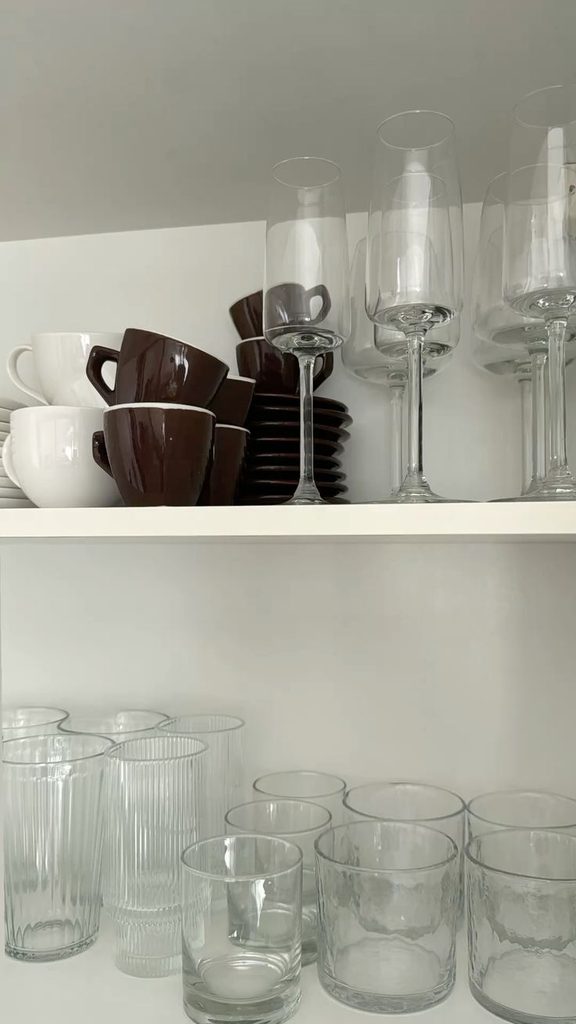 Several simple drinking glasses arranged neatly on a kitchen shelf