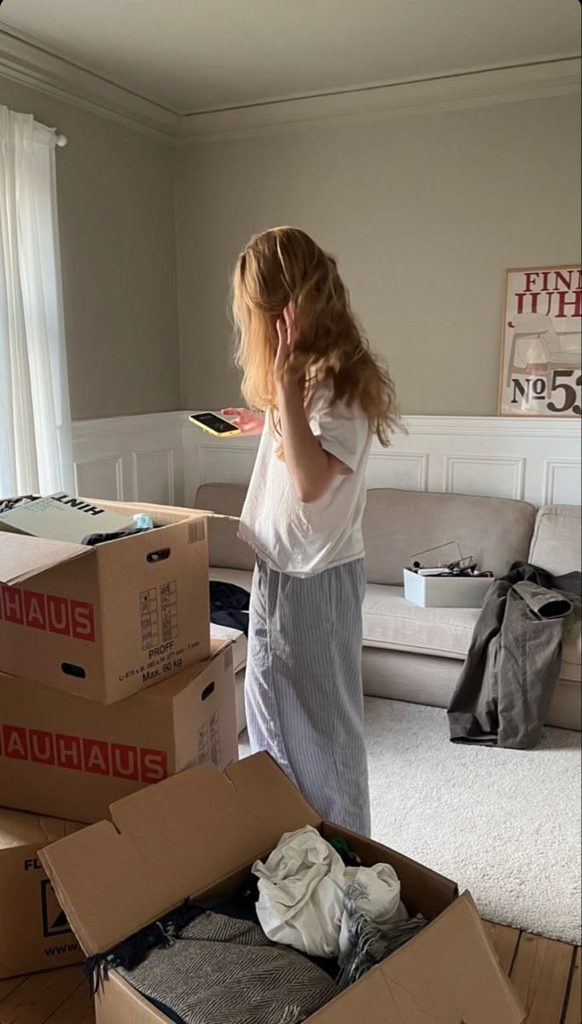 Young lady standing in a simple new apartment surrounded by a few moving boxes