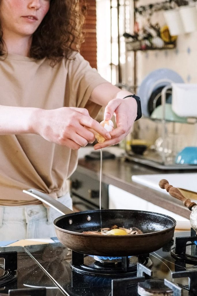 Young adult cooking eggs in a frying pan on a small kitchen stove as part of first apartment essentials