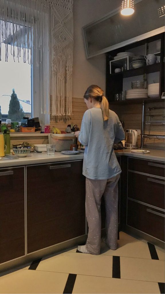 A young adult standing in a simple kitchen surrounded by everyday things