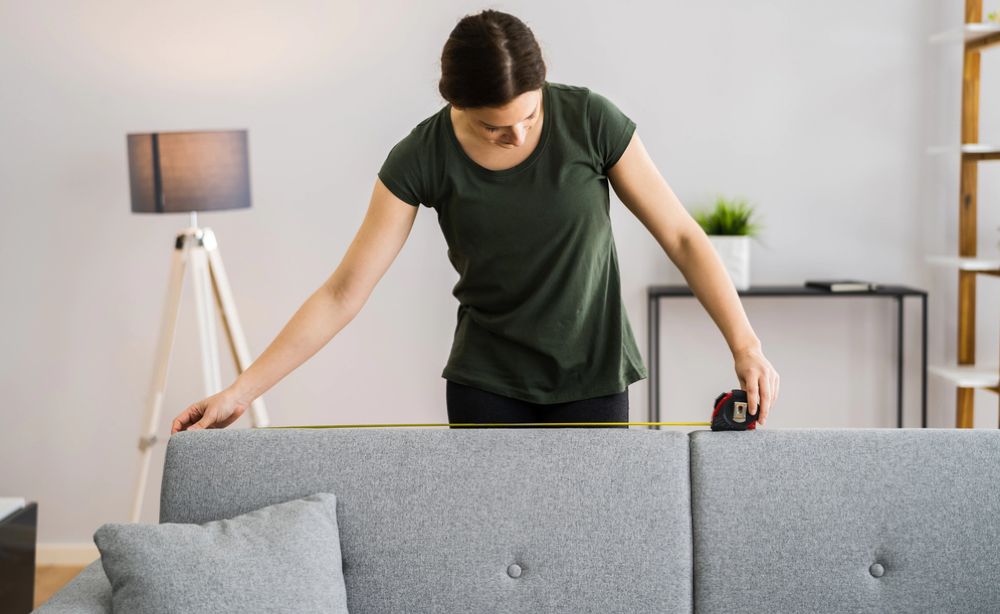 A young adult using a measuring tape to check a sofa
