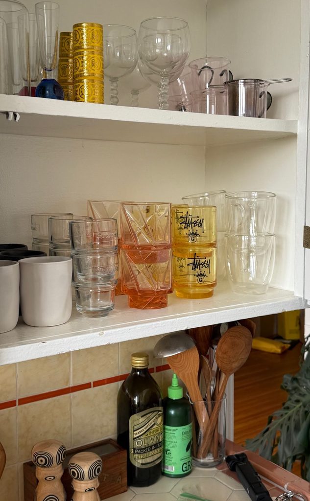 Everyday drinking glasses and reusable cups arranged neatly on a kitchen shelf.