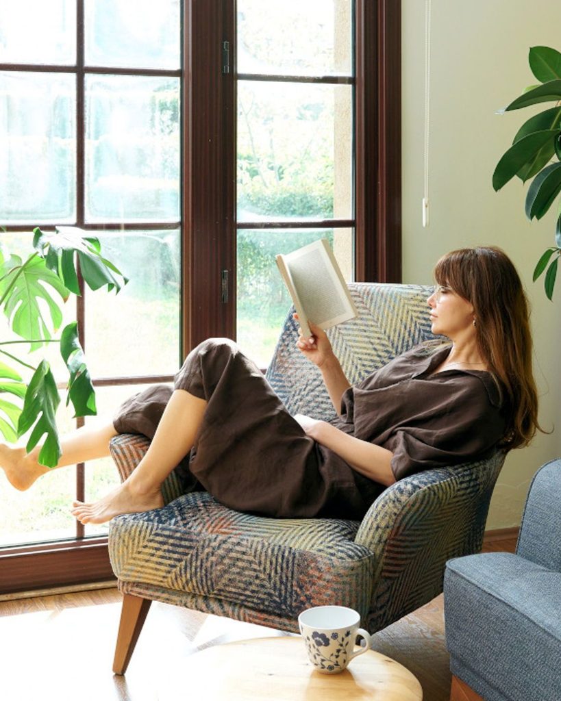 A young adult sitting in a simple apartment while reading a book