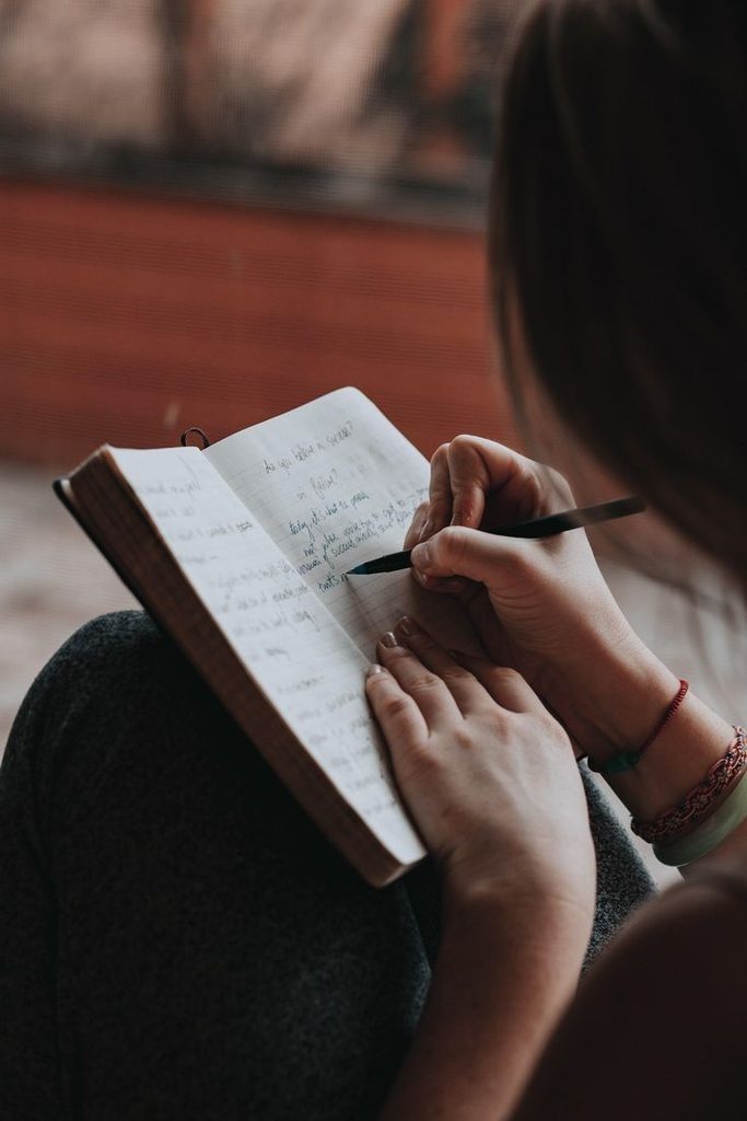 A young adult looking through an old notebook and writing down things